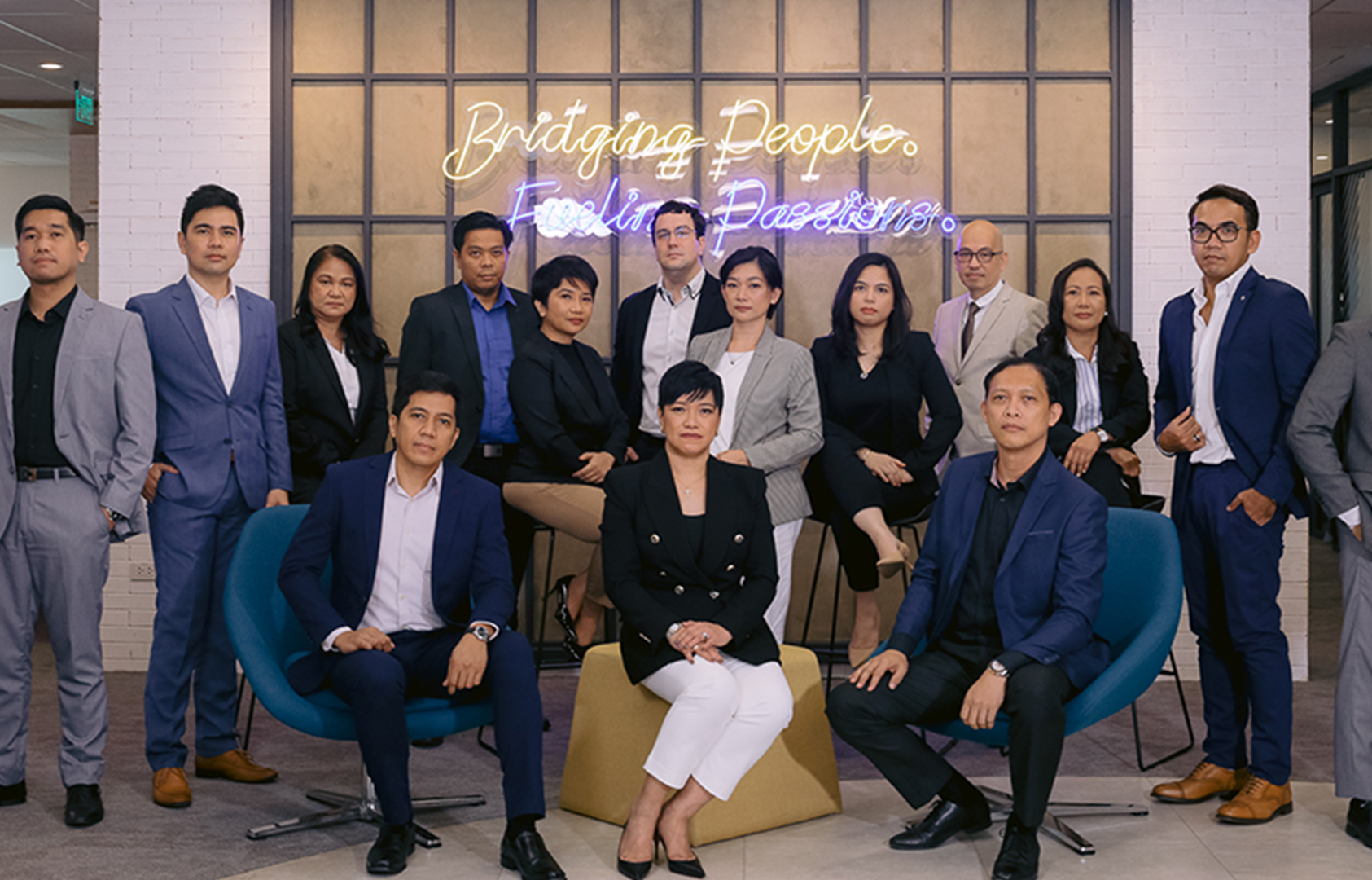 A group of asian filipino business people standing in front of a lit up wall in their office.